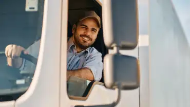 Happy professional truck driver driving his truck and looking at camera